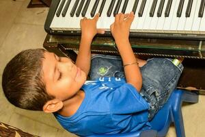 asiático chico jugando el sintetizador o piano. linda pequeño niño aprendizaje cómo a jugar piano. niño manos en el teclado interior. foto