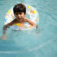 Happy Indian boy swimming in a pool, Kid wearing swimming costume along with air tube during hot summer vacations, Children boy in big swimming pool. photo