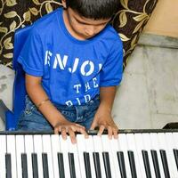 asiático chico jugando el sintetizador o piano. linda pequeño niño aprendizaje cómo a jugar piano. niño manos en el teclado interior. foto