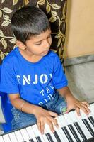 Asian boy playing the synthesizer or piano. Cute little kid learning how to play piano. Child's hands on the keyboard indoor. photo