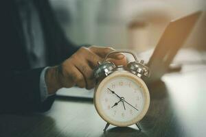selectivo atención de alarma reloj en escritorio cerca negocio hombre utilizando ordenador portátil a trabajando tiempo extraordinario para fecha límite a hogar, concepto de hora gestión. negocio concepto. foto