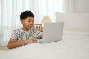 asiático chico utilizando ordenador portátil a hacer deberes a hogar foto