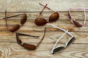 Different sunglasses on wooden background. Reflection of clouds and trees in sunglasses. Toned image. photo