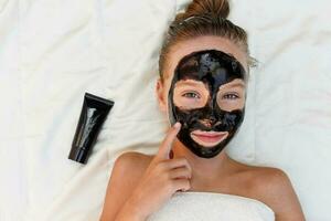 Beautiful girl with facial black clay mask. photo