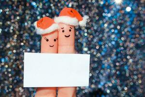 Finger art of couple celebrates Christmas. Concept of man and woman laughing in new year hats. Happy pair showing white blank page. Toned image. photo