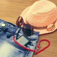 Summer women's accessories red sunglasses, beads, denim shorts, mobile phone, headphones, a sun hat. Toned image photo