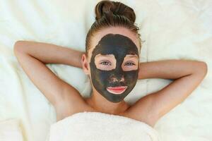 Beautiful girl with facial black clay mask. photo