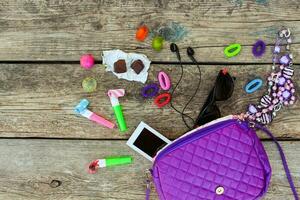 Children's handbag and accessories mobile phone, hair bands, candy, beads, headphones, sunglasses on old wooden background. Top view. Toned image. photo