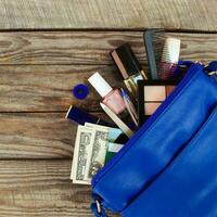 Things from open lady handbag. women's purse on wood background. Cosmetics, money and women's accessories fell out of the blue handbag. photo