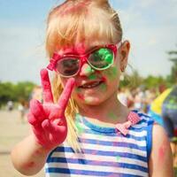 Happy girl shows sign victory with holi paint. photo