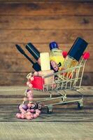 Shopping cart with cosmetics, beads on the old wood background. Toned image. photo