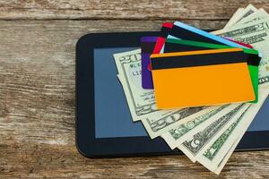 Credit card, dollars, computer tablet on wooden background. Top view. photo