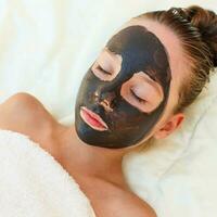 Beautiful girl with facial black clay mask. photo