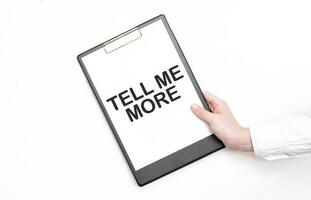 A businessman holds a folder with paper sheet with the text TELL ME MORE. Business concept. photo
