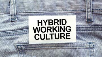 Text HYBRID WORKING CULTURE on a white paper stuck out from jeans pocket. Business concept photo