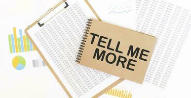 Text TELL ME MORE on brown paper notepad on the table with diagram. Business concept photo