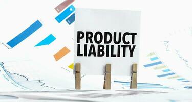 Text product liability on paper sheet with chart, dice, spectacles, pen, laptop and blue and yellow push pin on wooden table photo