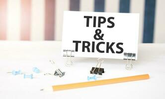 TIPS AND TRICKS sign on paper on white desk with office tools. Blue and white background photo