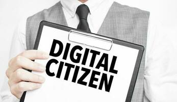 DIGITAL CITIZEN inscription on a notebook in the hands of a businessman on a grey background, a man points with a finger to the text photo