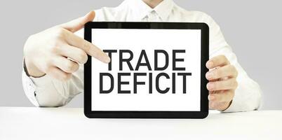 Text TRADE DEFICIT on tablet display in businessman hands on the white background. Business concept photo