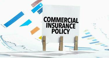 Text commercial insurance policy on paper sheet with chart, dice, spectacles, pen, laptop and blue and yellow push pin on wooden table photo