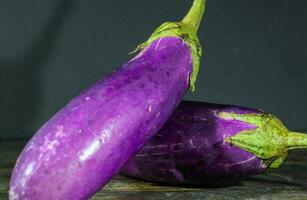 Bright Purple Fresh healthy eggplants on dark wooden background photo