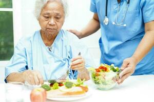 asiático mayor mujer paciente comiendo salmón estaca y vegetal ensalada para sano comida en hospital. foto