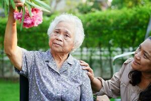 Asian elderly woman enjoy in flower garden with caregiver in park. photo