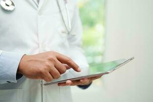 Asian man doctor using tablet computer to reading patient report, check up and search for solve treatment health medical online in hospital. photo