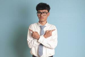 confuso mayor alto colegio estudiante vistiendo blanco camisa uniforme con gris Corbata con cruzado manos, señalando oblicuo, haciendo elección, elegir Entre dos opciones aislado imagen en azul antecedentes foto