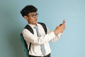 Indonesian senior high school student wearing white shirt uniform with gray tie showing shocked face expression while holding a mobile phone. Isolated image on white background photo