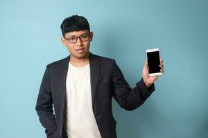 Portrait of young Asian business man in casual suit showing and holding phone. Isolated image on blue background photo