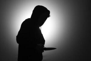 Mysterious man wearing black hoodie holding a knife to stab someone. Crimes and criminality concept photo