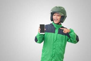 Portrait of Asian online taxi driver wearing green jacket and helmet showing and presenting blank screen mobile phone. Isolated image on white background photo