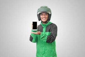 Portrait of Asian online taxi driver wearing green jacket and helmet showing and presenting blank screen mobile phone. Isolated image on white background photo