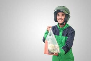 Portrait of Asian online taxi driver wearing green jacket and helmet delivering the vegetables from traditional market and pointing with finger. Isolated image on white background photo