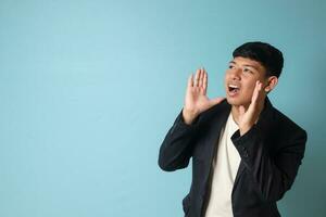 Portrait of young Asian business man in casual suit shouting to the distance. Isolated image on blue background photo