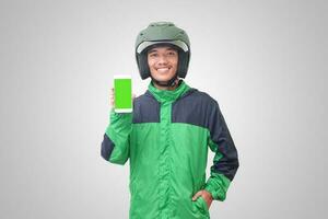 Portrait of Asian online taxi driver wearing green jacket and helmet showing and presenting blank screen mobile phone. Isolated image on white background photo