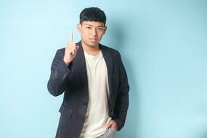 Portrait of young Asian business man in casual suit pointing upward while looking at camera. Isolated image on blue background photo