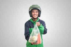 retrato de asiático en línea Taxi conductor vistiendo verde chaqueta y casco entregando el vegetales desde tradicional mercado y señalando con dedo. aislado imagen en blanco antecedentes foto