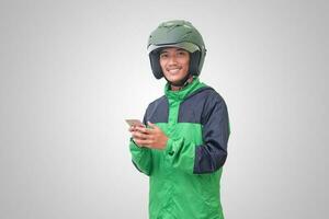 Portrait of Asian online taxi driver wearing green jacket and helmet holding a mobile phone and smiling. Advertising concept. Isolated image on white background photo