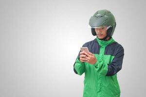 Portrait of Asian online taxi driver wearing green jacket and helmet holding a mobile phone and smiling. Advertising concept. Isolated image on white background photo