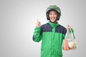 retrato de asiático en línea Taxi conductor vistiendo verde chaqueta y casco entregando el vegetales desde tradicional mercado y señalando con dedo. aislado imagen en blanco antecedentes foto