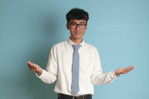 Confused senior high school student wearing white shirt uniform with gray tie spreading his hands sideways and holding two things, demonstrate products. Isolated image on white background photo