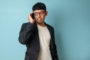 Portrait of young Asian business man in casual suit smiling while talking on the phone. Isolated image on blue background photo