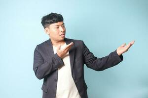 Portrait of young Asian business man in casual suit presenting something with both hands and looking at it. Isolated image on blue background photo