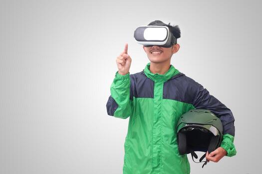 Portrait of Asian online taxi driver wearing green jacket and holding a helmet while using virtual reality or VR and pointing. Isolated image on white background photo
