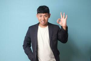 Portrait of young Asian business man in casual suit agreeing at something with happy expressions. Isolated image on blue background photo