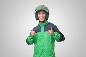 Portrait of Asian online taxi driver wearing green jacket and helmet showing good job sign, thumb up. Isolated image on white background photo