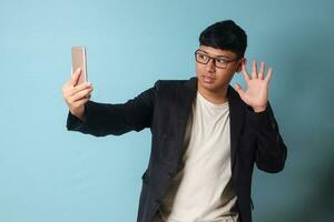 Portrait of young Asian business man in casual suit taking a selfie with confident and happy expression. Isolated image on blue background photo